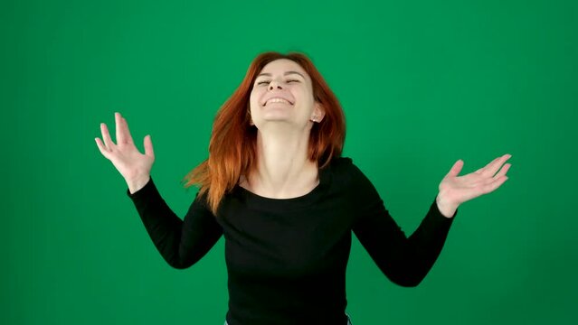 Sincere laughter, a woman laughs, smiles, spreads her arms to the side, raising her head up, happiness, joy, on a green background, beautiful people, red hair, black clothes, incredible happiness.
