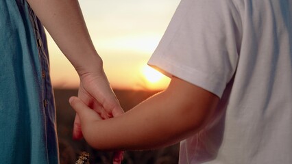 Child and mother share hands in front of sun. Closeup mother lets go of child hand, separation....
