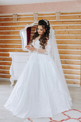 Fototapeta premium A wonderful beautiful portrait of a young bride. Beautiful bride with wedding makeup and jewelry wreath on long curly hair. Wedding photo model with brown eyes in a beautiful interior.