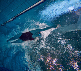 Bubbles. Young woman in swimsuit, cap and goggles training, practicing, swimming in pool indoors. Concept of pool sports, water sport, competition, active lifestyle