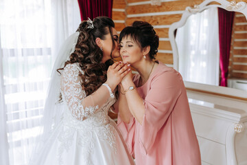 A beautiful and happy mother and her daughter, the bride, are standing next to each other. The best day for parents. Tender moments at the wedding.