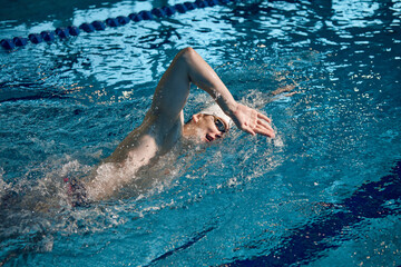 Professional athlete. Young man, swimming sportsman in motion, wearing cap and goggles swimming in pool. Concept of pool sports, water sport, competition, active lifestyle