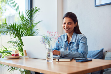 Smiling woman using laptop in cafe working remotely