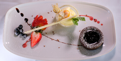 chocolate fondant on white plate with dark chocolate ice cream strawberries drops of syrup...