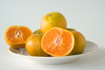 Pile of oranges in a plate on a white background. There is one fruit that was cut in half.