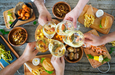 People with white wine toasting over served table with food.