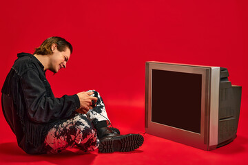 Young man sitting in front of retro TV with blank screen and trying to play videogames with gamepad...