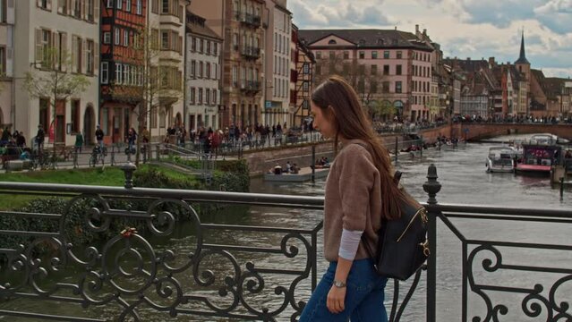 Tracking shot of young woman walking along Strasbourg river Petite France old french architecture buildings on a beautiful sunny day 