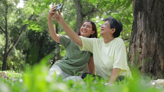 Asian family. Mother and daughter sit and relax in the garden, use their smartphones to take photos together. Caring for the elderly to be happy in retirement. happy time