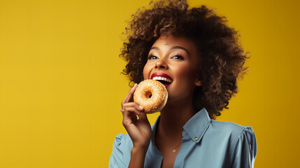 portrait of a african american woman holding eating donut isolated on yellow background, junk unhealthy food diet concept copy space, Valentine day, sweet tasty life - obrazy, fototapety, plakaty