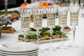 buffet table, white tablecloth, champagne glasses on a long stem. Carbonated white wine. Selective focus, plates and snacks. The concept of a coffee break for corporate parties and new year events.