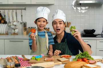 Happy moment asian father and son cooking breakfast in the kitchen. Dad and child asian family having fun preparing food bread egg sandwich. Positive parent and kid nice relationship