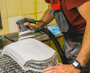 Fototapeta premium Restoration of the headlight glass using a grinding machine. A man polishes the optics of a car's headlights with a polishing machine at a service station. Hands working with a polishing machine.