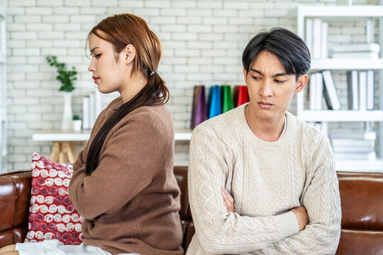 Photo of resentful asian guy and girl acting like arguing couple and not speaking to each other, while sitting together on couch at home