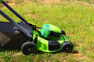Mowing is performed by man using an electric lawn mower on green grass