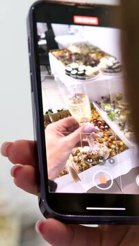 filming food on a phone, close-up, a woman hand with a smartphone films a glass of champagne against the backdrop of buffet snacks, a young unrecognizable woman presses to take a photo