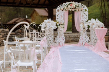 Wedding decor. Many white chairs and a white path. A white and pink arch decorated with flowers. Preparation for the wedding ceremony. Celebration