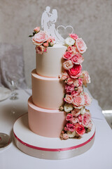 A large luxurious multi-tiered wedding cake is decorated with fresh pink rose flowers in the banquet hall. Wedding dessert under the evening light. Wedding decor.