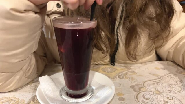 non-alcoholic mulled war mixed with straws in a glass glass with orange delicious hot drink of cherry juice with seasonings on the hand ring red lips loose hair jacket. in winter drink