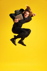 Fototapeta na wymiar Young man, dressed smart casual, fashion and glasses outfit jumping of joy and happiness holding laptop against yellow background. Concept of work, study, success in career development, betting. Ad