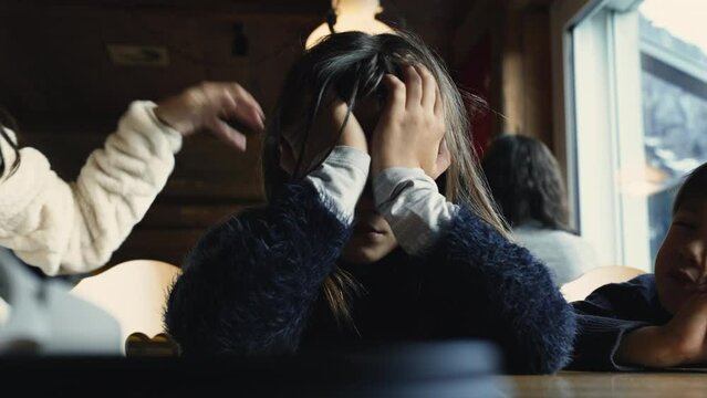 Tired bored little girl covering face with hands at restaurant diner, sad child feels exhausted and boredom