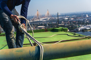 High rise worker preparing safety rope knot on rooftop before doing highrise cleanning service in...