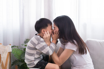 Happy family Asian mother and son playing together touching cheeks each other laughing out loud kidding with fun indoor at home weekend holiday, mom and kid bonding relationship, motherhood tenderness