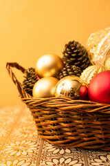 Imagen vertical de una canasta navideña decorada con esferas en una mesa y fondo amarillo 