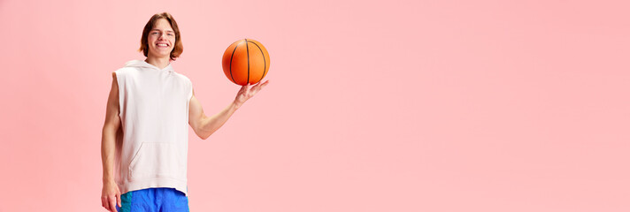 Sportsman,, young basketball player dressed retro uniform and spins ball on one finger against pink background with negative space to insert text. Concept of active lifestyle, sport, recreation, hobby