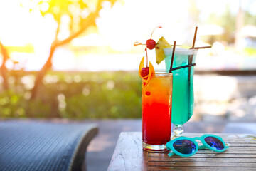 Glass with a bright blue lagoon and tequila sunrise cocktails by the pool