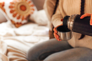 Female hands pouring tea or coffee from thermos to cup in trailer