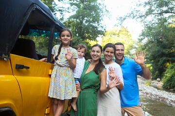 Happy smiling family with kids by the car with mountain river background. Portrait of a smiling family with children in country