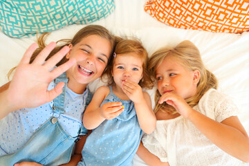 Three happy little sisters on a bed having fun