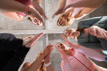 Obraz premium The image offers an uplifting perspective of a group of women in a huddle, viewed from below. Their upraised hands meet in the center, symbolizing unity and collective motivation. The women are