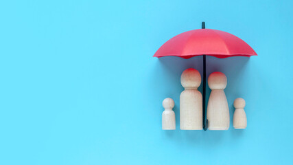 Family health and life insurance concept. Wooden people represent parent and children under a red umbrella. - obrazy, fototapety, plakaty