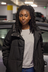 A young Black woman stands poised in an urban parking garage, her style effortlessly blending...