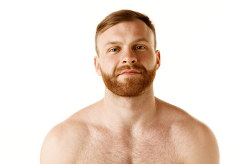 Portrait of young attractive shirtless man with red head and bear looking at camera against white...