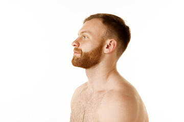 Fototapeta premium Side view portrait of young handsome redhead man with beard and bare shoulders looking away against white studio background. Concept of natural beauty, youth, spa treatment, selfcare, cosmetic. Ad