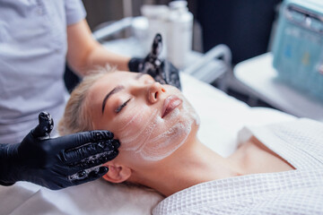 Close up portrait of a young beautiful woman getting facial clecing procedure before face massage