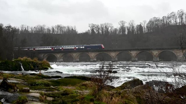 Rhine Falls, Switzerland, 12 23 2022: An electric train crosses an old bridge over the Rhine Falls.