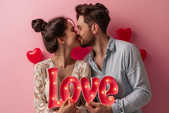 Love concept image with lovely man and woman couple kissing and glowing love sign and pink background