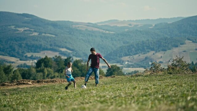 Father and Son Playing Football Together on a Mountain Meadow on a Sunny Day. Concept of Aspiring Athlete