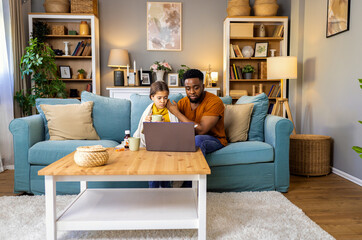 African American father and daughter with fever sitting at home and have online consultations with...