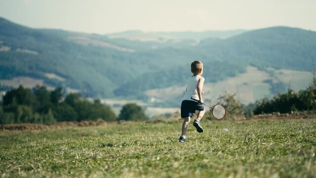Little Blond Child Running with a Badminton Racket Across a Mountain Meadow