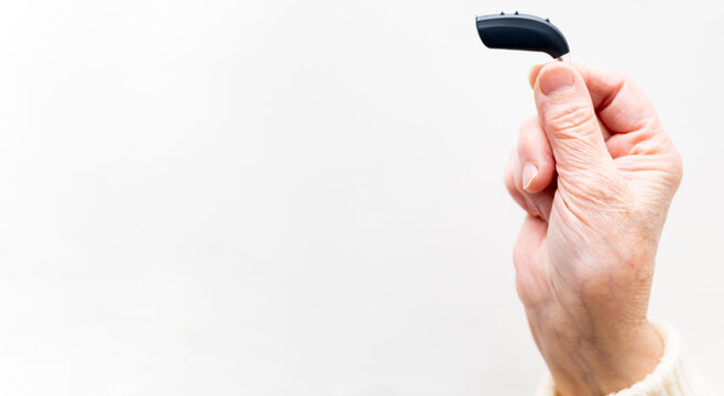 Photo of an elderly person's hand holding a behind-the-ear hearing aid on a white background. Sound amplifier. Retroaural.Copyspace for advertising for hearing aids.