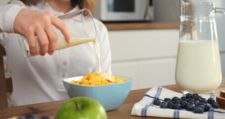 Girl pours milk into cereal in slow motion scene healthy eating in modern kitchen Healthy eating...