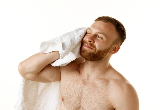 Portrait of young attractive man with naked torso drying off after shower with towel against white studio background. Concept of natural beauty, selfcare hygiene, male facial care, body care. Ad - Powered by Adobe