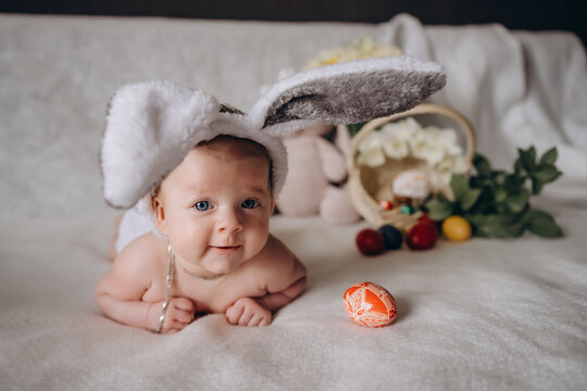 Cute little baby smiles wearing bunny ears for Easter. Near Easter eggs.