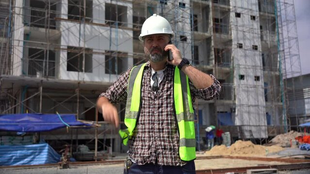 Senior architect or civil engineer talking to phone pointing finger to inspection and control at construction site. building project