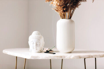 Small marble table with little buddha head statue and burning incense stick on stand